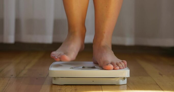 A woman measures her weight on white scale on floor, measuring tape falls off