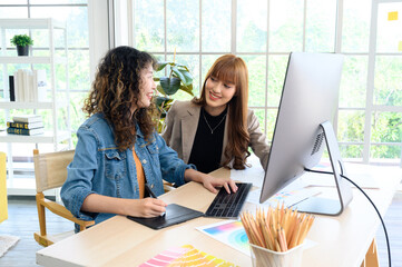 Fototapeta premium Happy two young female graphic designers discussing with colleague in office. Creative people working together using computer at desk.