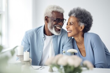 Smiling, dark-complected stylish Black elderly couple, looking away, at table in kitchen with white walls, in the style of professional stock photography, photo-realistic, high exposure, low contrast - Powered by Adobe