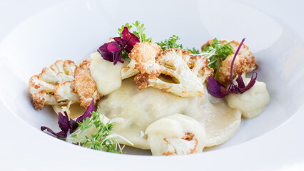 Close up of ravioli with mushrooms, horseradish and cauliflower on white plate