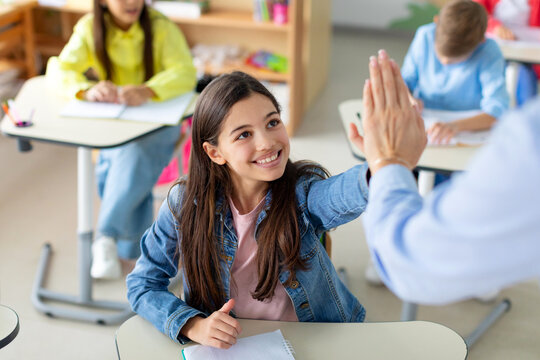 Happy kid girl giving high five to female teacher in classroom. Teacher encouraging helping child student giving support during elementary junior school lesson