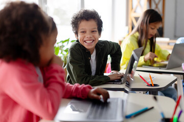 Schoolboy using laptop at lesson, actively discussing and collaborating with friend, highlighting the contemporary approach to interactive learning