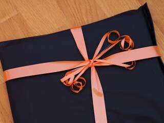 A black gift with an orange bow on a wooden background.