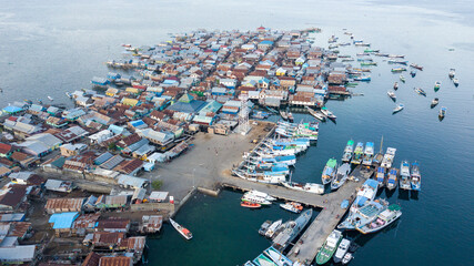 Aerial view of a bustling fishing village with colorful rooftops, surrounded by boats in the water.