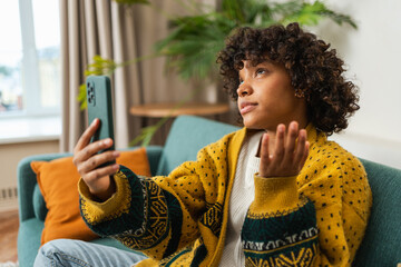 African American girl holding smartphone having video chat. Female blogger chatting with best friends in social network. Young woman having virtual meeting online chat video call at home - obrazy, fototapety, plakaty
