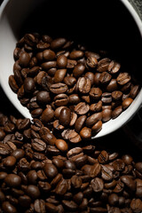 Large roasted coffee beans poured from a ceramic cup onto the table