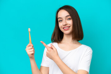 Young Ukrainian woman brushing teeth isolated on blue background and pointing it
