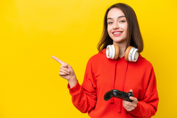 Young Ukrainian woman playing with a video game controller isolated on yellow background pointing finger to the side © luismolinero
