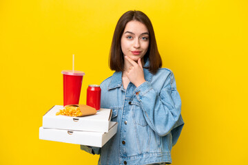 Young Ukrainian woman holding fast food isolated on yellow background thinking