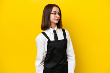 Young Ukrainian waitress woman isolated on yellow background looking to the side