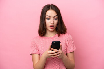 Young Ukrainian woman isolated on pink background looking at the camera while using the mobile with...