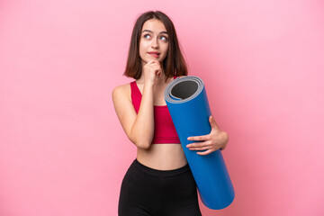 Young sport Ukrainian woman going to yoga classes while holding a mat isolated on pink background...