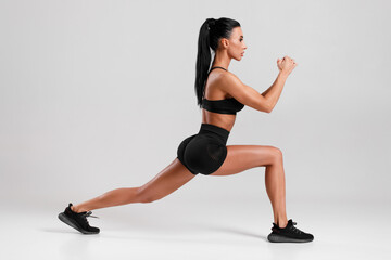 Fitness woman doing lunges exercises for leg muscle workout training. Active girl doing front forward one leg step lunge exercise, on gray background