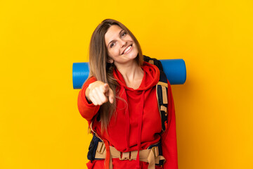 Slovak mountaineer woman with a big backpack isolated on yellow background pointing front with happy expression