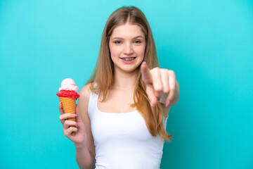 Teenager Russian girl with a cornet ice cream isolated on blue background points finger at you with...