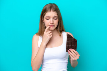 Teenager Russian girl isolated on blue background taking a chocolate tablet and having doubts