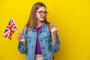 Teenager Russian girl holding an United Kingdom flag isolated on yellow background pointing to the side to present a product