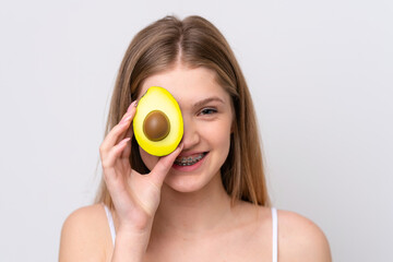 Teenager Russian girl isolated on white background holding an avocado while smiling. Close up portrait