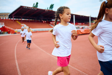 Fototapeta premium Little girl running during sports training at stadium.