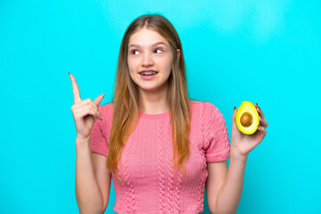 Teenager Russian girl holding an avocado isolated on blue background intending to realizes the solution while lifting a finger up - obrazy, fototapety, plakaty