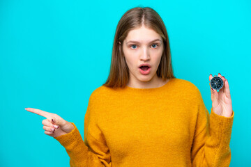 Teenager Russian girl holding compass isolated on blue background surprised and pointing side