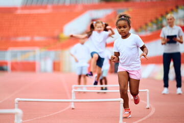 Black little girl running on track during sports training at stadium.