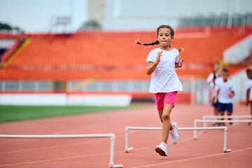Small girl running on track with obstacles at athletics club.