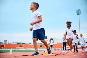 Obraz premium Black girl crossing agility ladder during PE class at stadium.