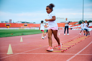 Obraz premium African American little girl running during exercise class at stadium.