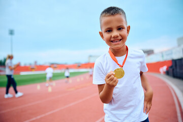 Happy boy holding golden medal after winning in sports race at stadium.