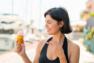 Young pretty Bulgarian woman with a cornet ice cream at outdoors and pointing it