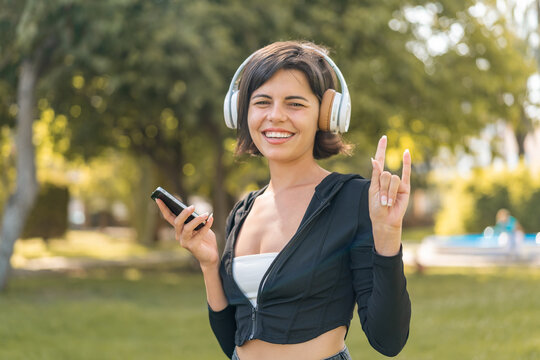 Young pretty Bulgarian woman at outdoors listening music with a mobile making rock gesture