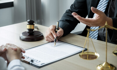 Lawyer hand holding pen and providing legal consult business dispute service at the office with justice scale and gavel hammer - obrazy, fototapety, plakaty