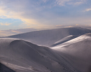 Fototapeta na wymiar Snow covered winter mountains in last evening sunlight. Magnificent windy dusk.