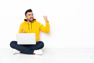 Caucasian man sitting on the floor with his laptop celebrating a victory