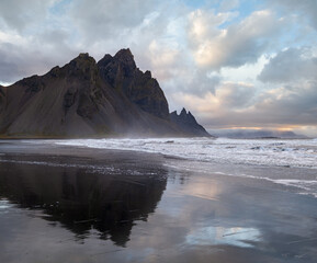 Sunrise Stokksnes cape sea beach and Vestrahorn Mountain with its reflection on wet black volcanic sand surface, Iceland. Amazing nature scenery, popular travel destination.