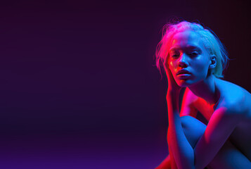 Nude young blonde woman in theatre pink spotlight, copy space on dark blue background