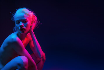 Nude young blonde woman in theatre pink spotlight, copy space on dark blue background - obrazy, fototapety, plakaty