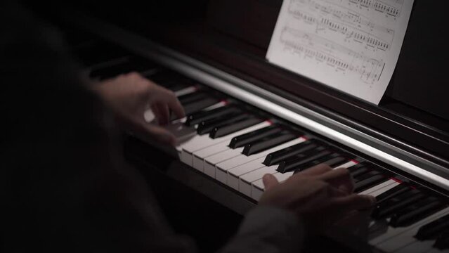 A pianist plays classical music on the piano while looking at the sheet music. A musician performs instrumental music in music classes. Shallow depth of field, blurred background.