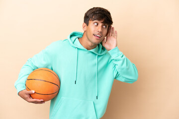 Handsome young basketball player man isolated on ocher background listening to something by putting...