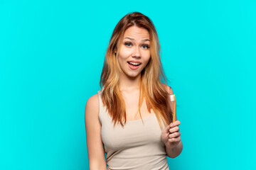 Teenager girl brushing teeth over isolated blue background with surprise facial expression