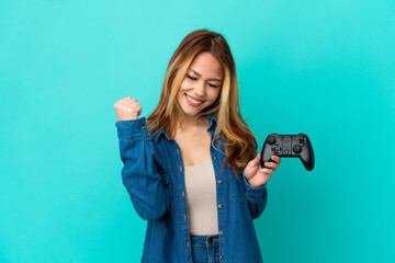 Teenager blonde girl playing with a video game controller over isolated wall celebrating a victory
