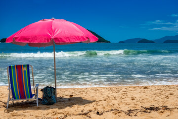 Beach day. Colorful beach chair under a pink umbrella on the beach sand on a sunny day with a blue sky