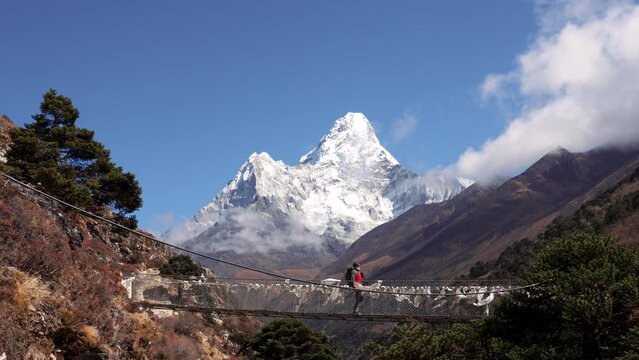 Tourists with backpacks walk along suspension bridge over gorge of Himalayan mountains background highest peaks in world. Trekking to Everest base camp in Nepal. Movement and achievement of goal