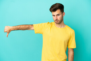 Young caucasian handsome man isolated on blue background showing thumb down with negative expression