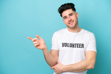 Young volunteer caucasian man isolated on blue background pointing finger to the side