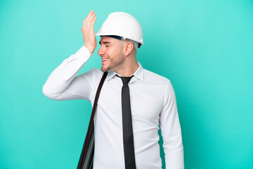 Young architect caucasian man with helmet and holding blueprints isolated on blue background has realized something and intending the solution