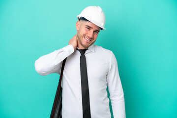 Young architect caucasian man with helmet and holding blueprints isolated on blue background laughing