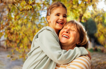 Little girl hugging smiling middle aged woman. Cute female kid and her grandmother enjoy walking outdoors