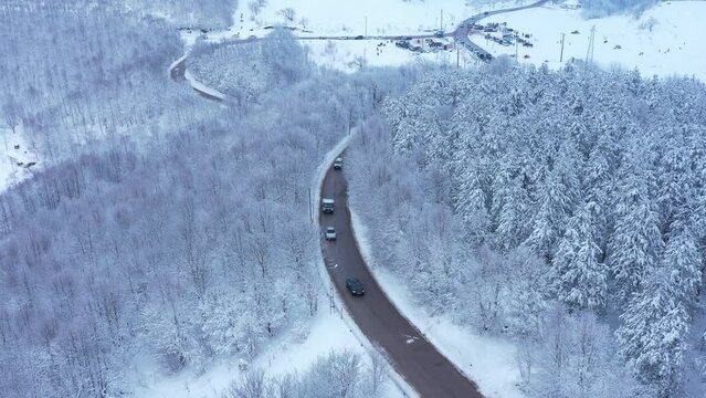Scenic drone footage of cars driving through a snow-covered forest in Turkey. Cars slowly following each other on the mountain road surrounded by snow covered trees on both sides near Bolu Kartepe. Dr